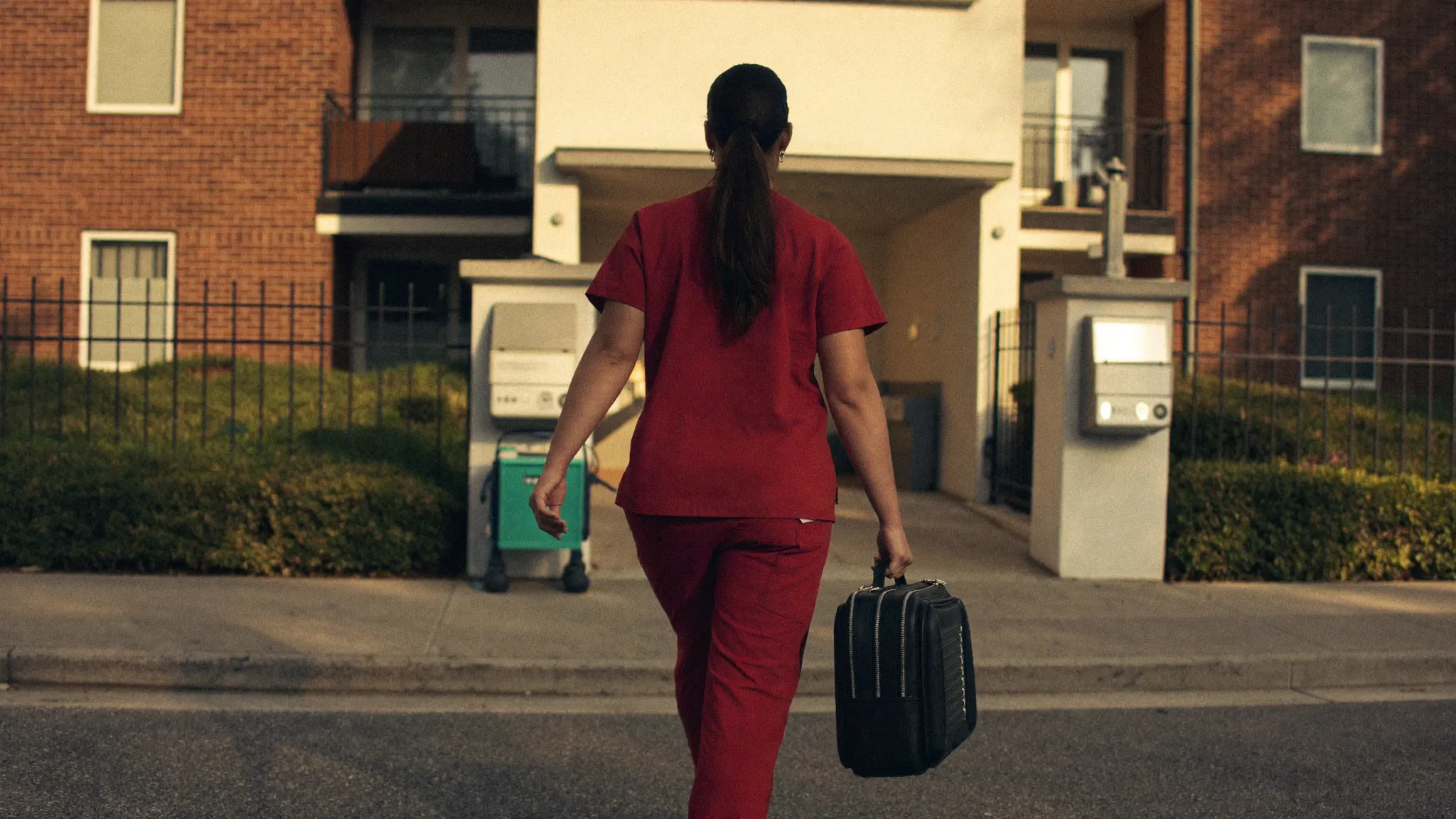 Asistentă medicală în uniformă roșie, cu geanta medicală în mână, ajungând la locuința unui pacient